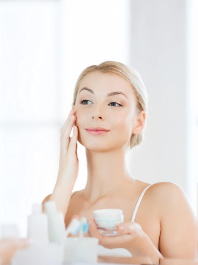 happy woman applying cream to face at bathroom